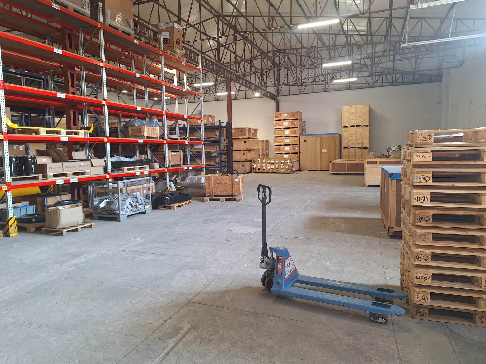 Operator moving palletised rail parts with an electric pallet jack between rack rows